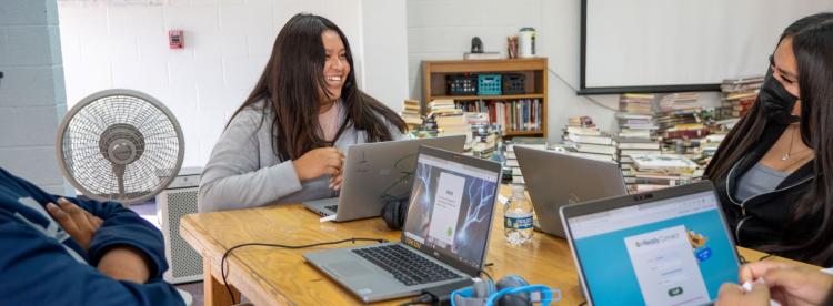 Three students work together at a table, each using their laptops for a group project.