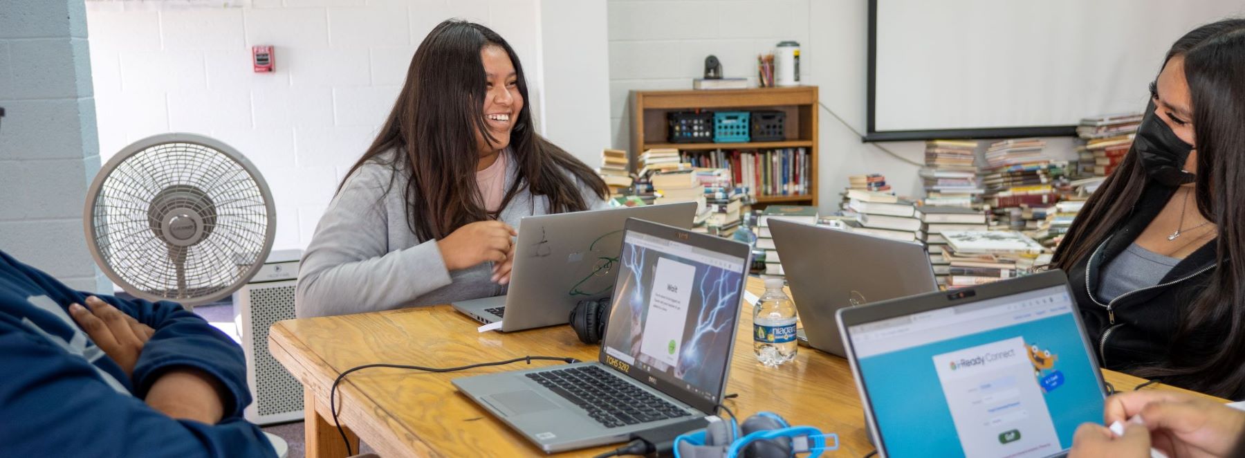 Three students work together at a table, each using their laptops for a group project.