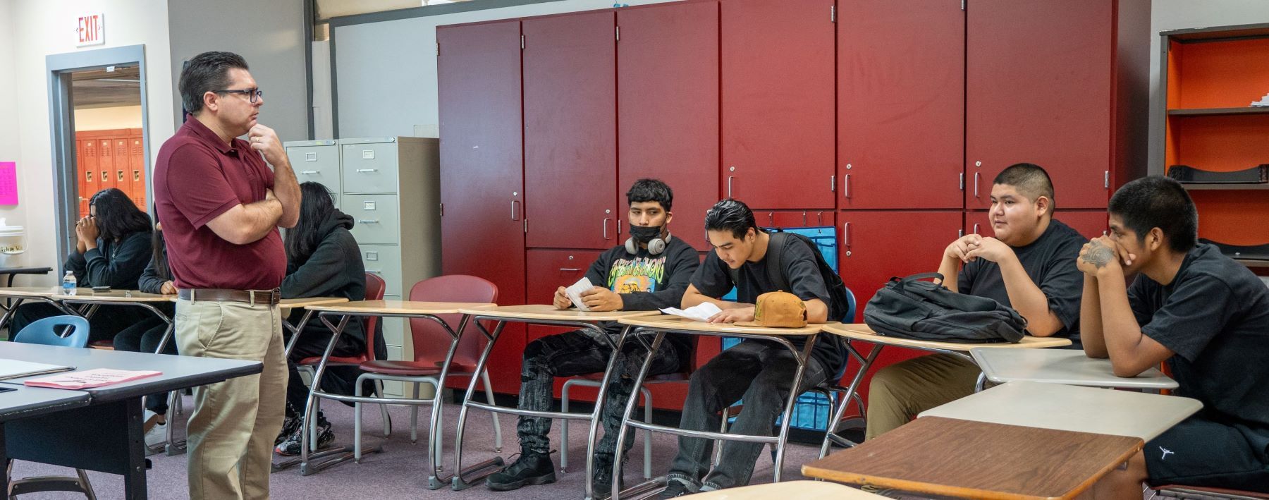 A teacher stands in front of students in a classroom, leading a discussion or lesson.