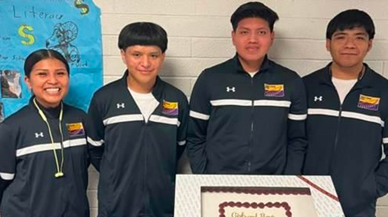 Four graduates standing in front of a cake.
